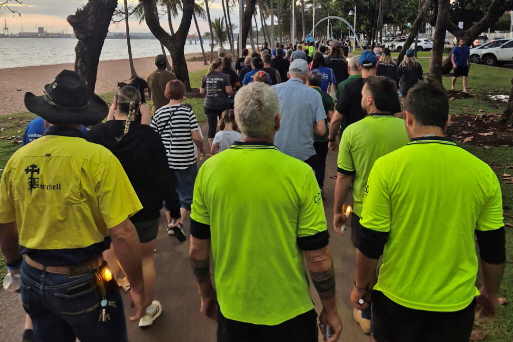 A large group of people walk along the strand boardwalk in Townsville