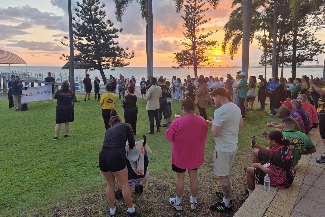 A group of people standing in a park beside the ocean at sunset
